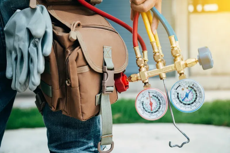 HVAC technician with service gauges and a tool backpack preparing to diagnose an air conditioning system